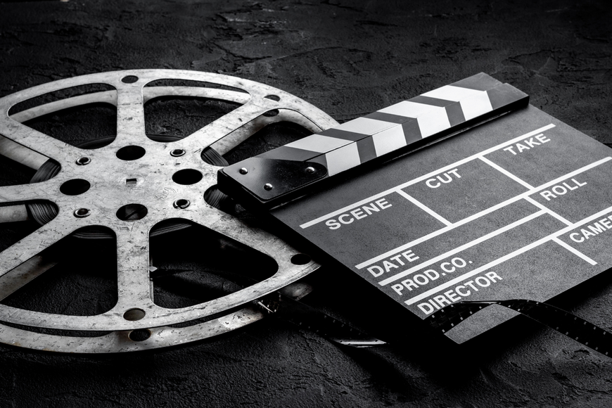 Film reel and clapperboard on a dark surface, with the clapperboard labeled scene, cut, take, and roll.