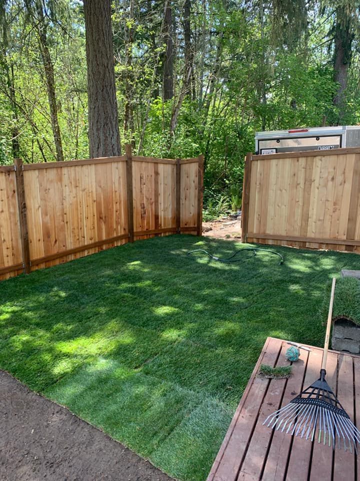 A wooden fence surrounds a lush green lawn in a backyard.