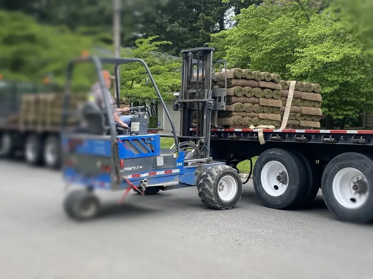 A forklift is pulling a trailer with a stack of grass on it.