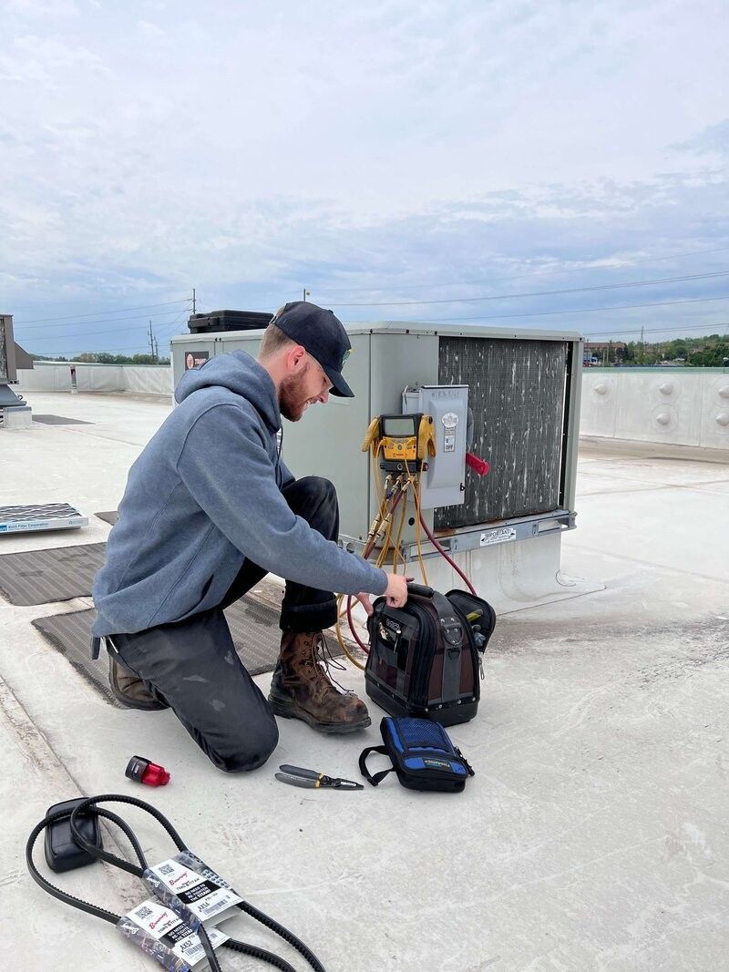 A Reston Contractor is kneeling down on a roof working on an air conditioner.
