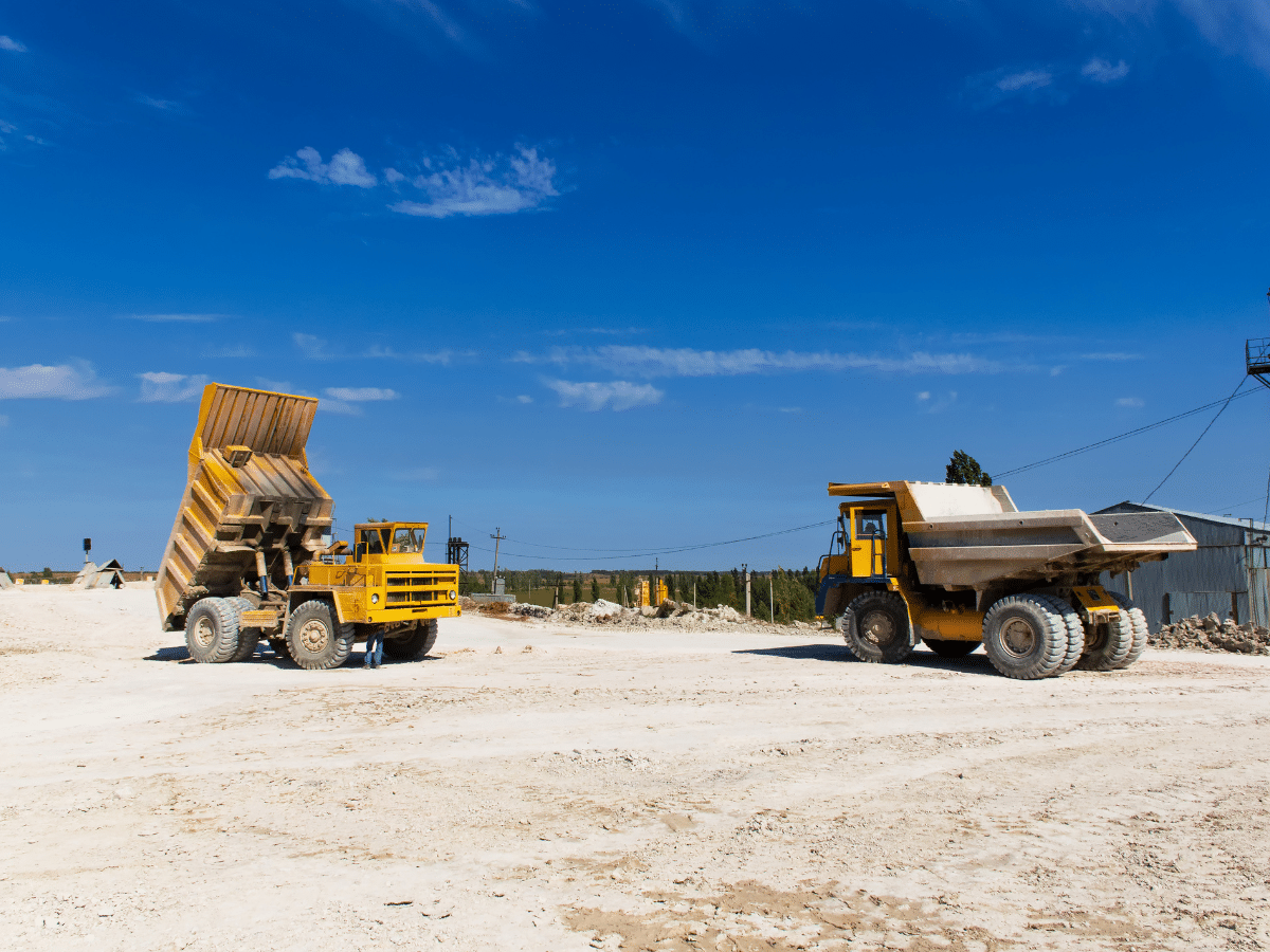 Two yellow mining dump trucks on a dusty white quarry under a bright blue sky