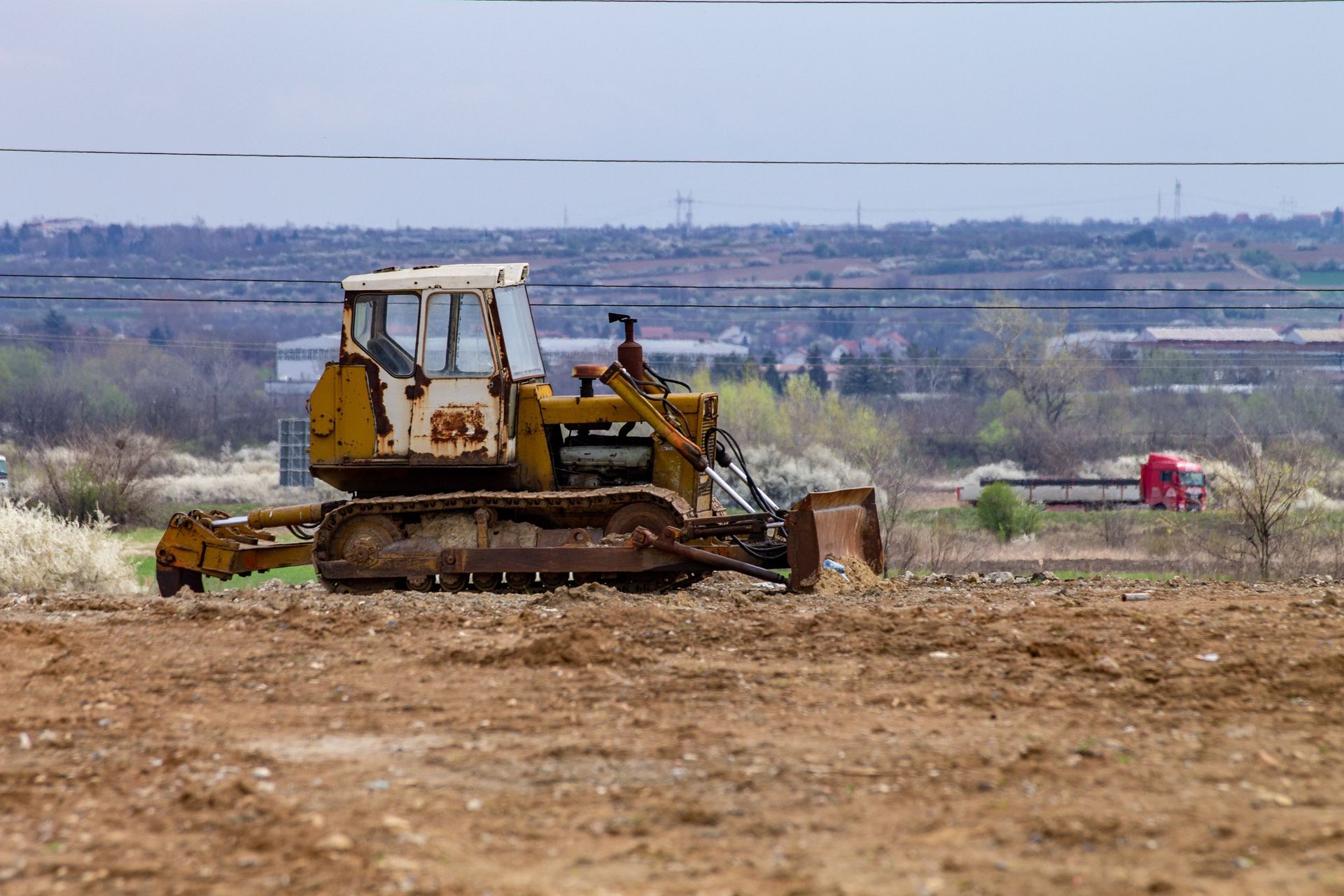 Construction worker in orange safety gear watching excavator demolish a concrete building amid rubble and dust
