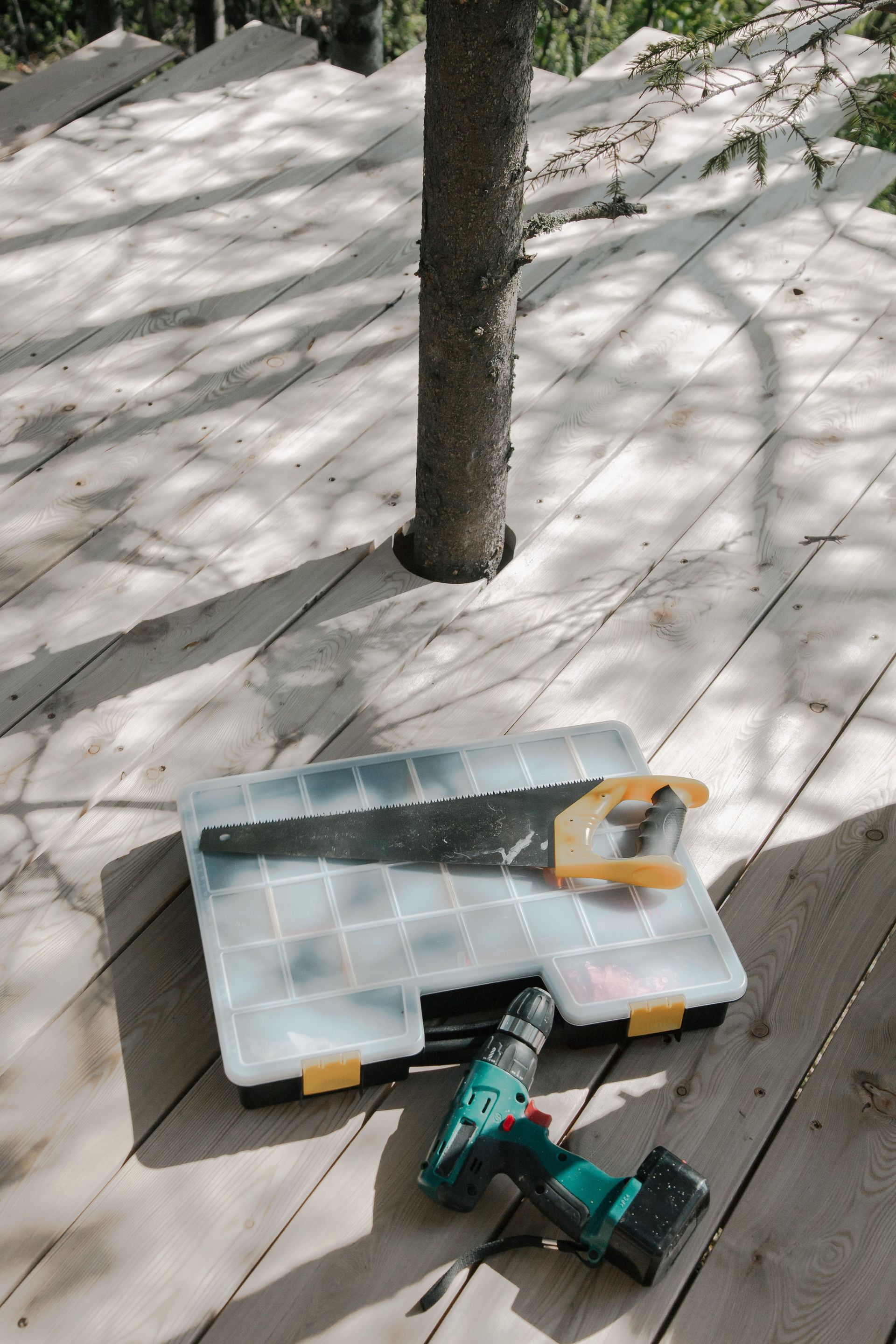 Power drill and toolbox on a wooden deck beside a tree, with snow in the background.