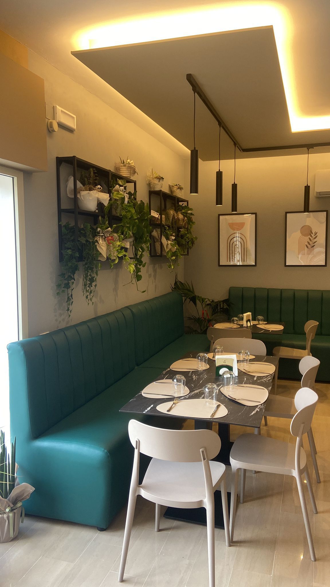 Interno del ristorante con sedute color verde acqua, tavoli neri e piante verdi.
