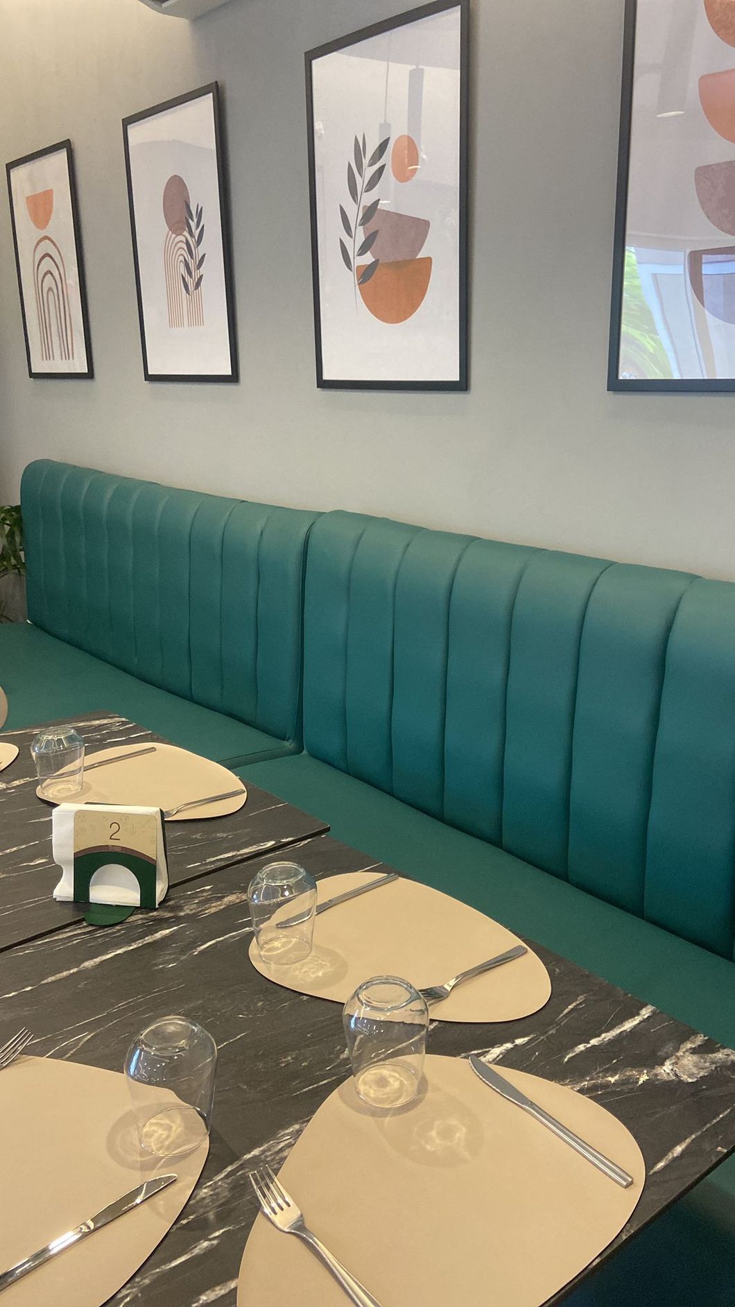 Interno di un ristorante con un lungo tavolo color verde acqua, tavoli apparecchiati per cenare e quadri astratti incorniciati alle pareti.