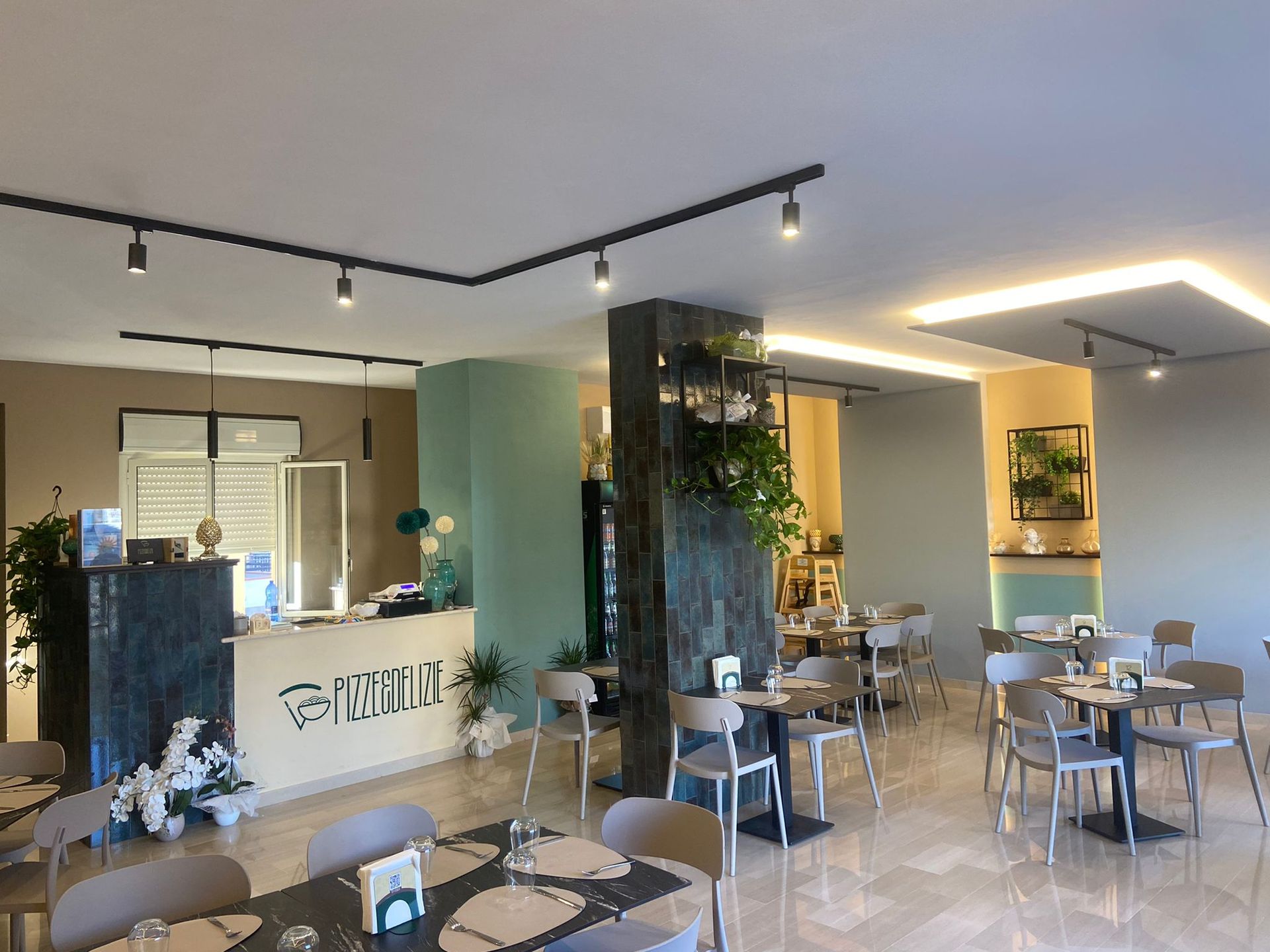 Interno di un ristorante moderno: tavoli, sedie, bancone, piante e lampade.