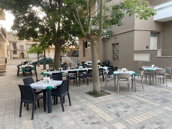 Area esterna con tavoli, sedie e alberi, possibilmente in una piazza cittadina.