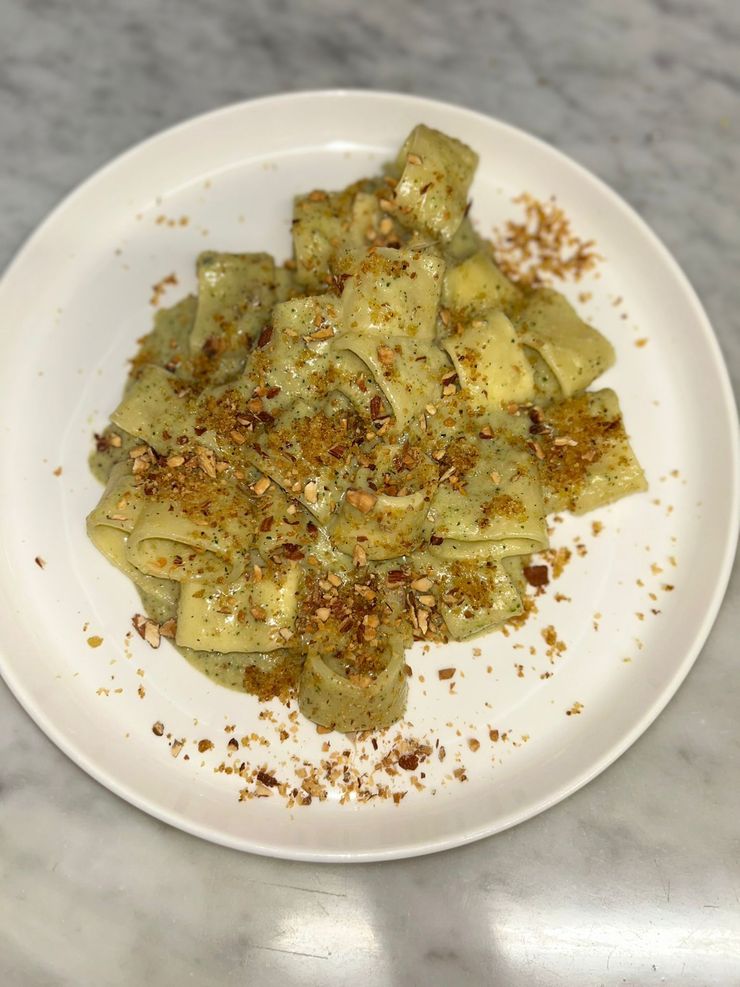 Piatto di pasta servito su un piatto bianco, ricoperto di salsa cremosa e guarnito con pangrattato tostato.