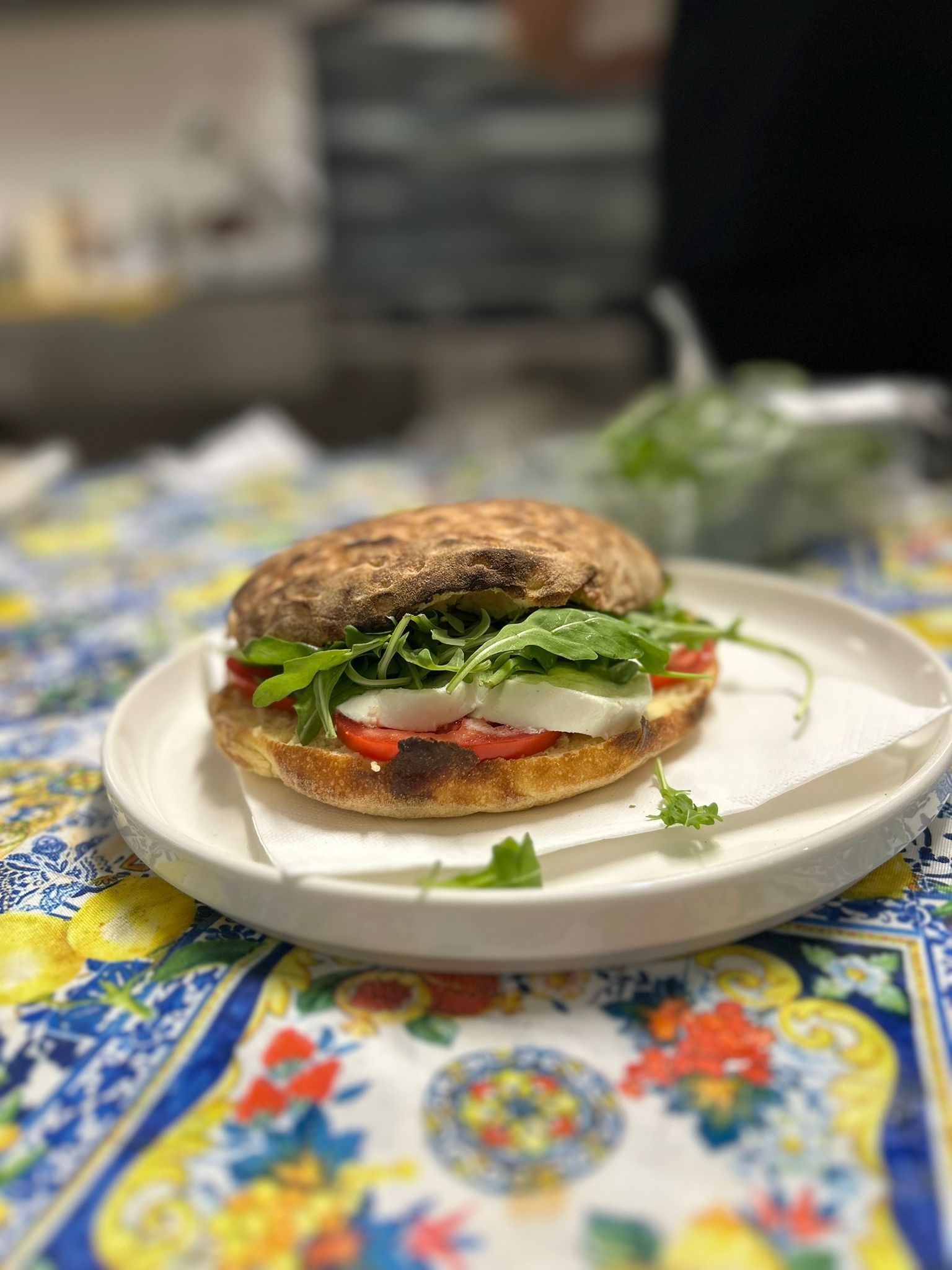 Panino con mozzarella, pomodoro e rucola su un piatto su una tovaglia colorata.