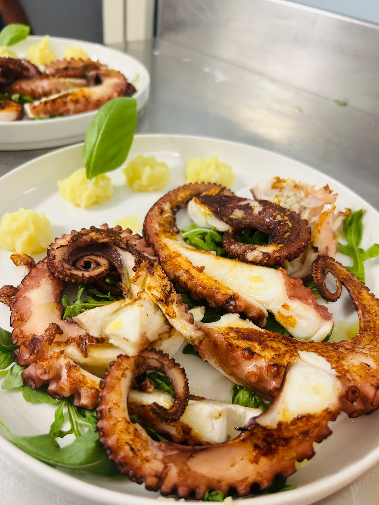 Polpo alla griglia su un piatto con purè di patate e basilico.