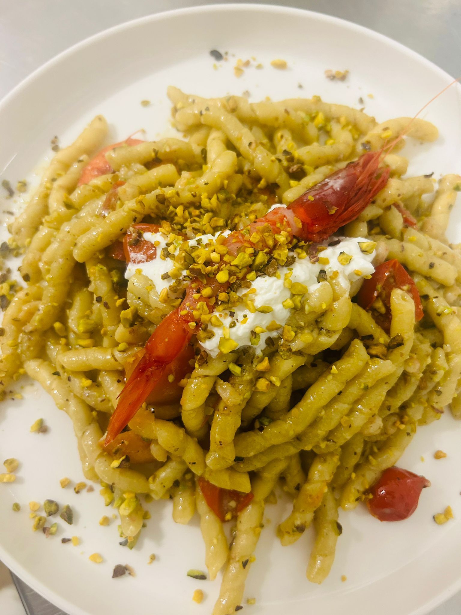 Piatto di pasta con gamberi, pomodori e pistacchi su un piatto bianco.