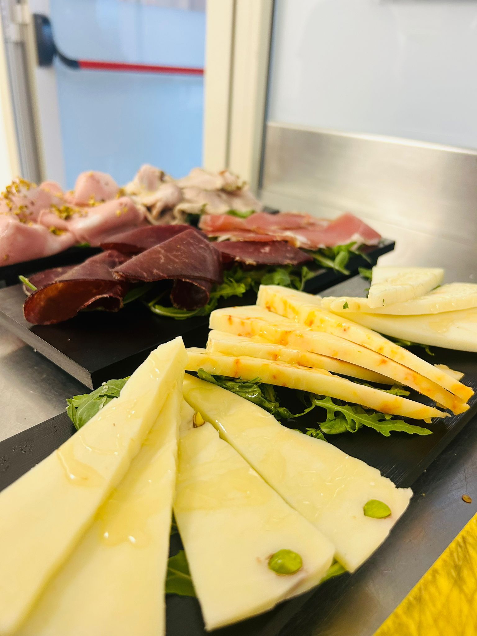 Tagliere di salumi e formaggi affettati, su un bancone di metallo.