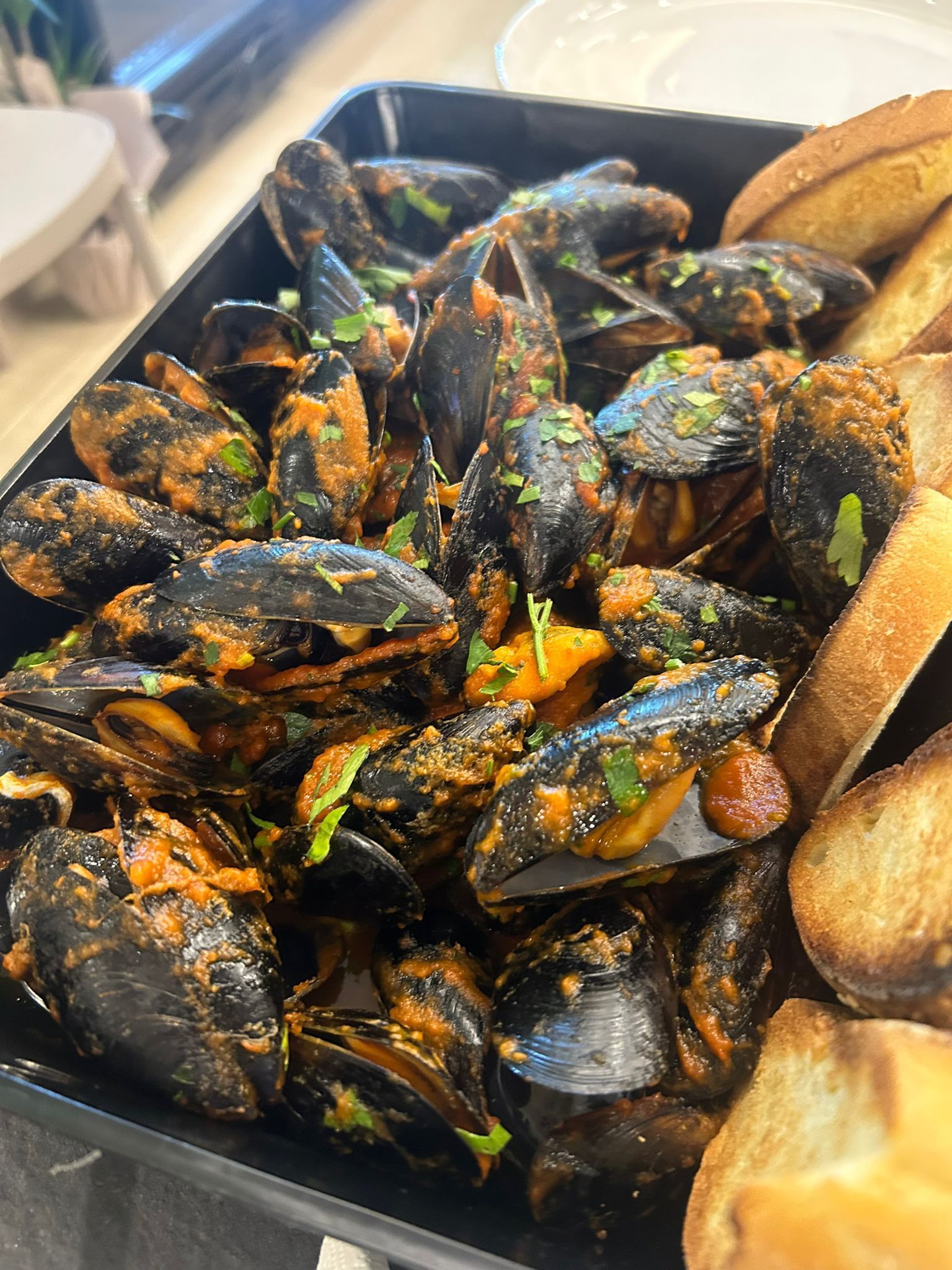 Cozze in salsa di pomodoro con pane tostato su un piatto.