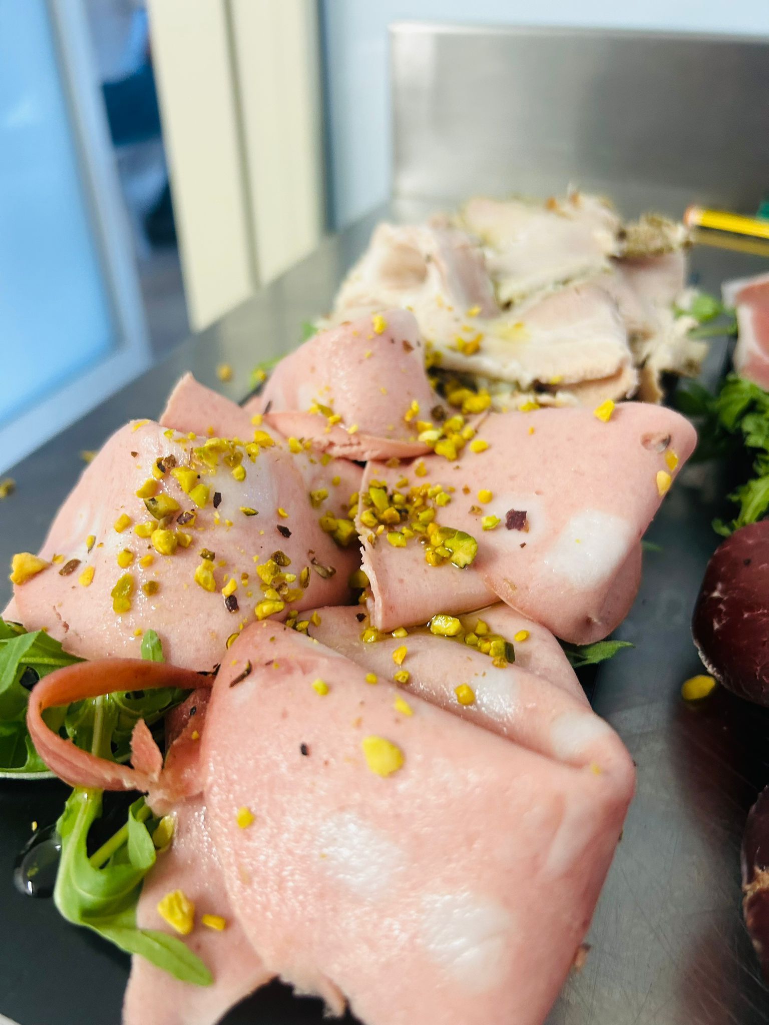 Fette di mortadella guarnite con pistacchi su un letto di verdure, servite con altre carni.