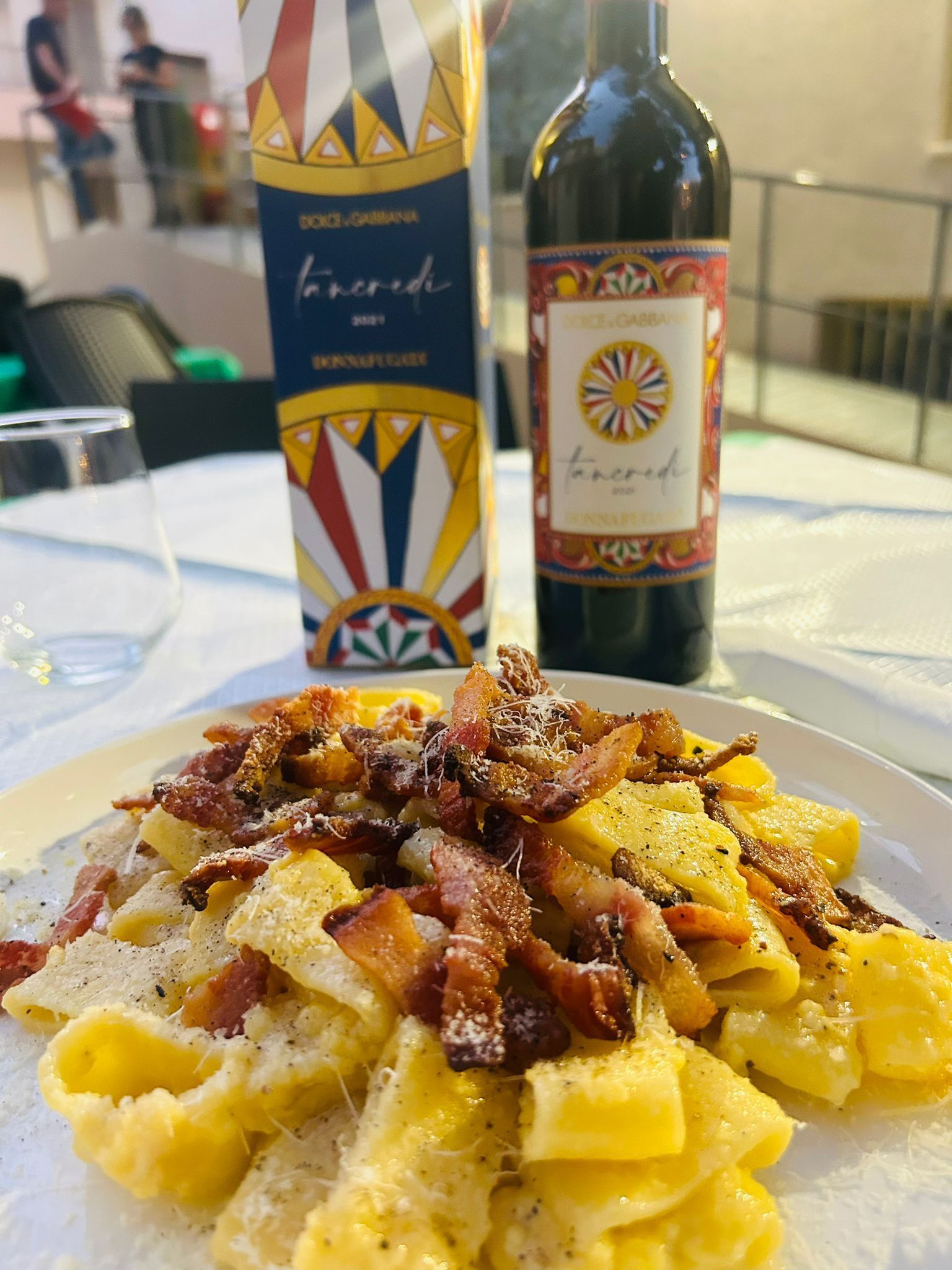 Pasta alla carbonara con pancetta croccante, accompagnata da una bottiglia e una scatola di vino italiano.