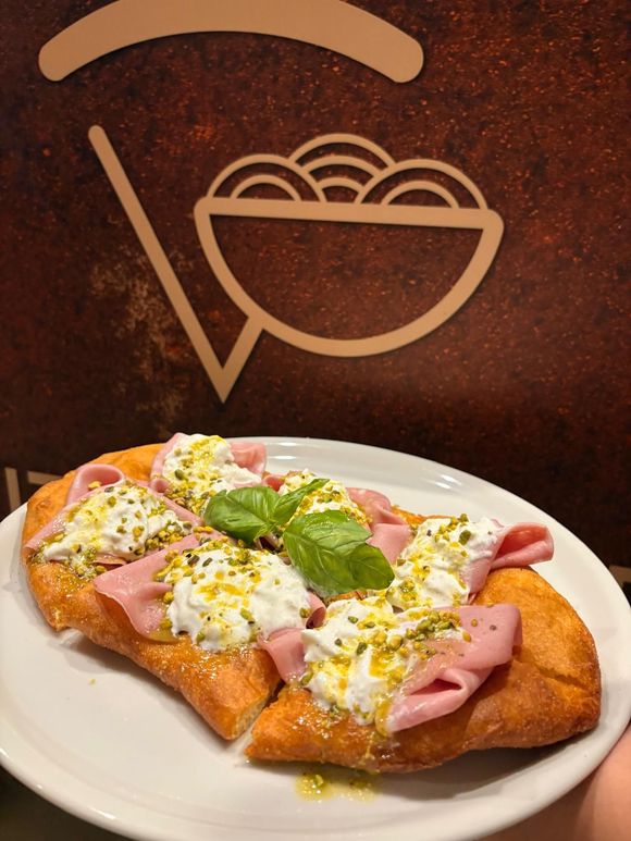 Pasta fritta condita con mortadella, formaggio, pistacchi e basilico, su un piatto.