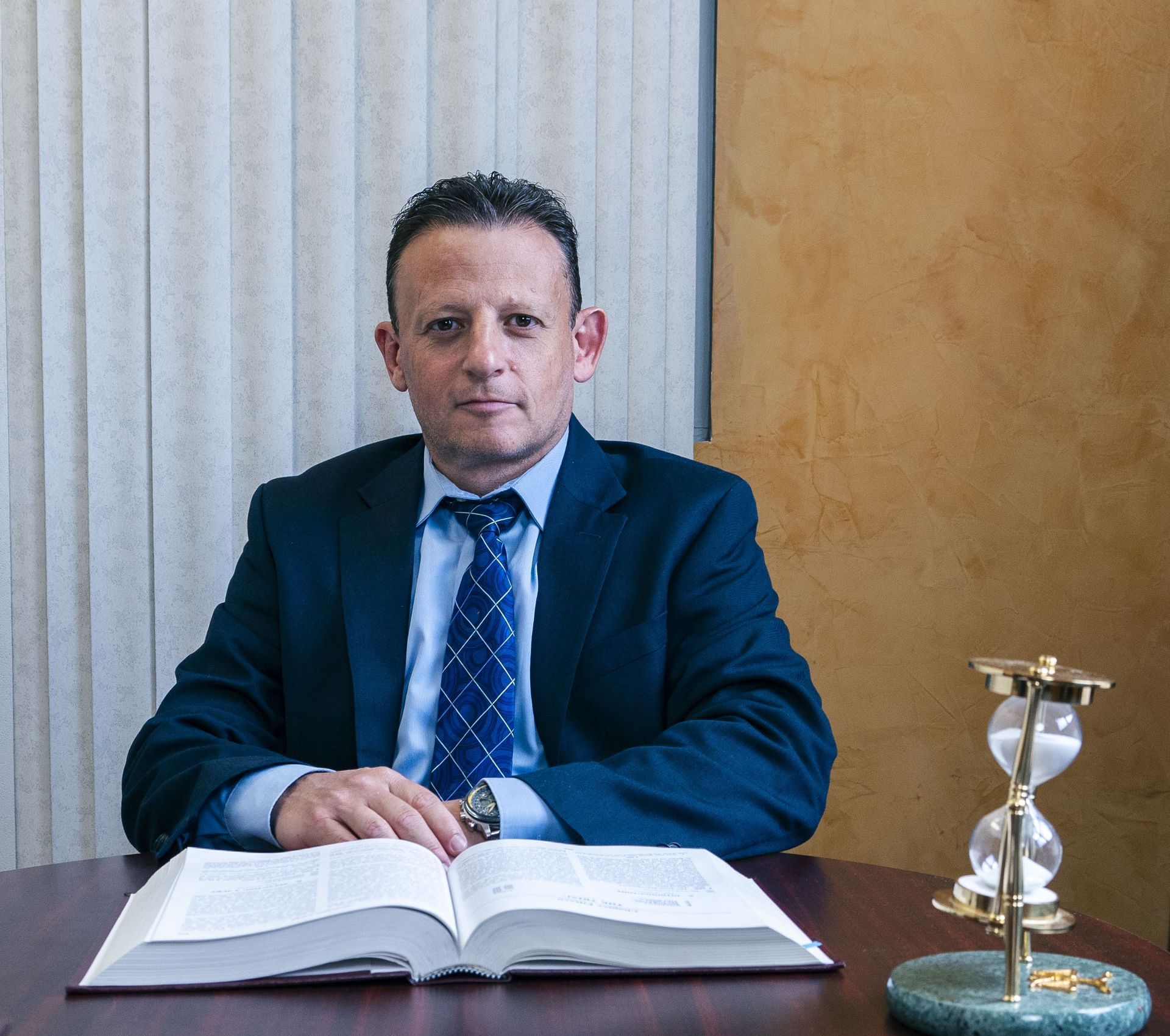 A man in a suit and tie is sitting at a desk reading a book
