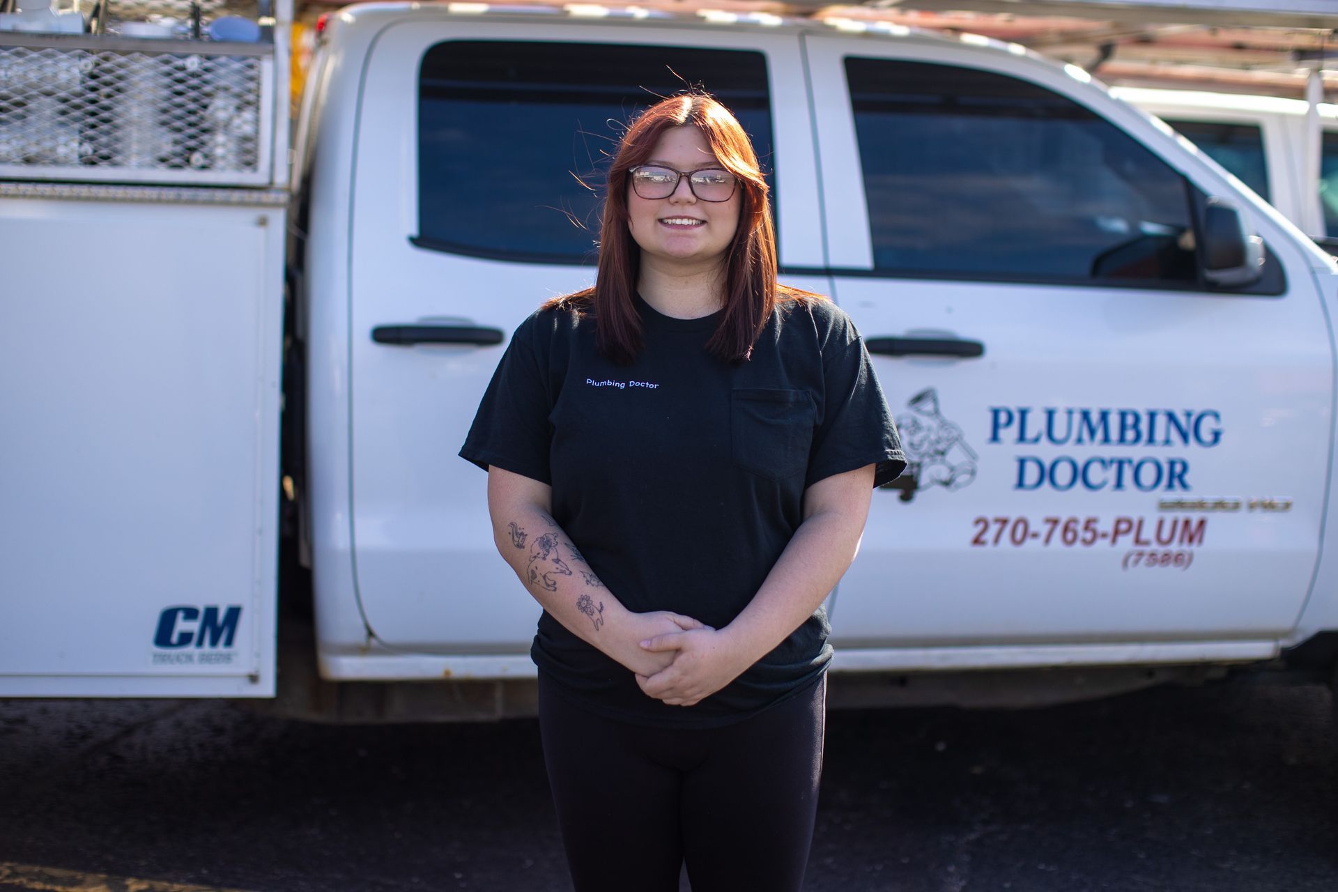 Woman in black shirt and glasses stands in front of a white truck with