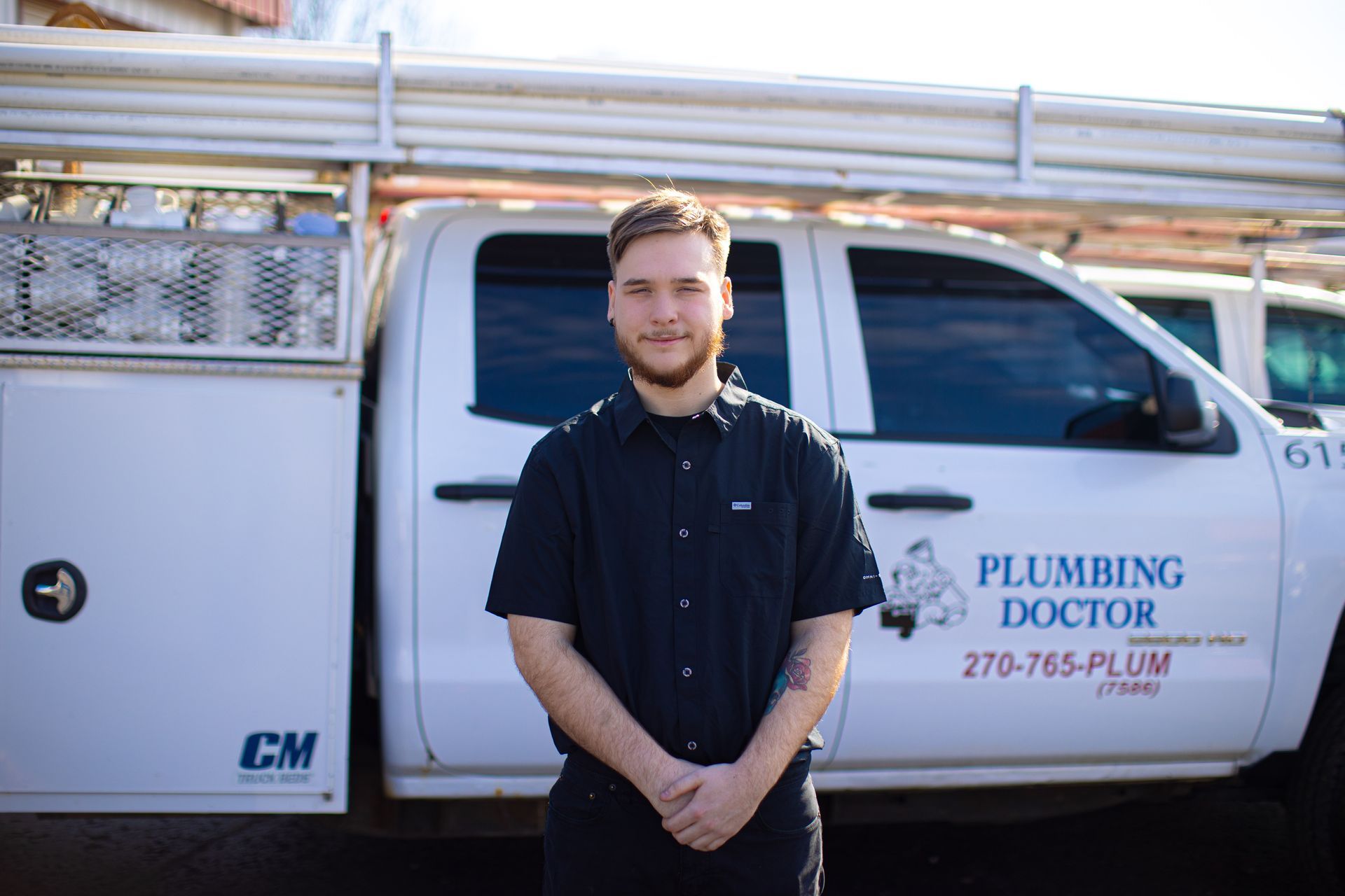 Man in black shirt stands near Plumbing Doctor truck.