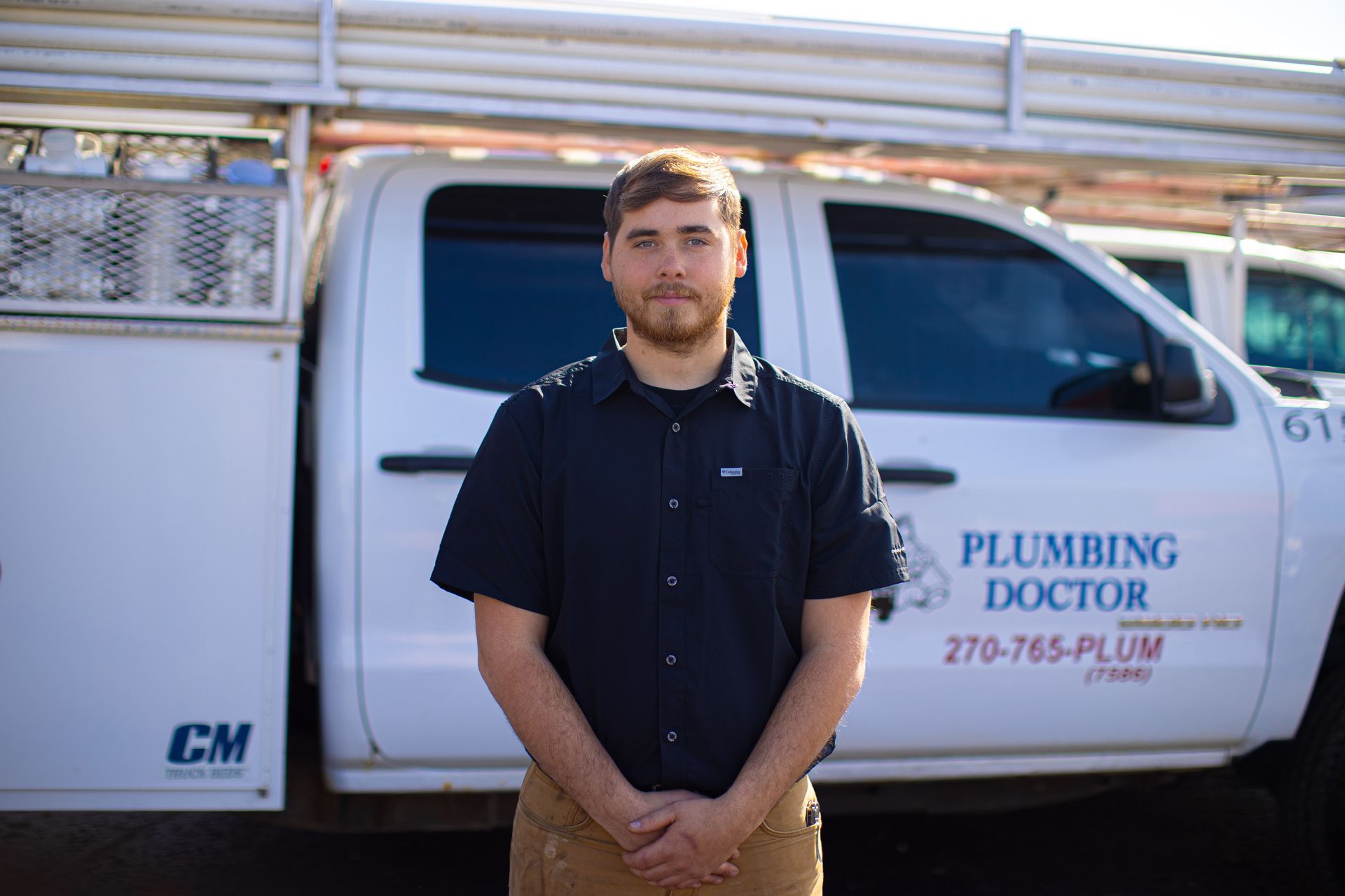 Man in front of a Plumbing Doctor truck, wearing a dark blue shirt and tan pants.