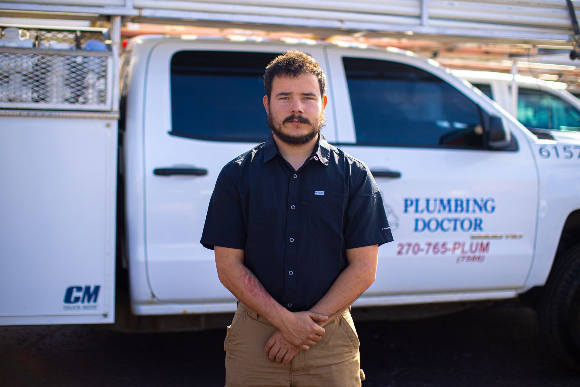 Man standing in front of a white plumbing truck, arms crossed.