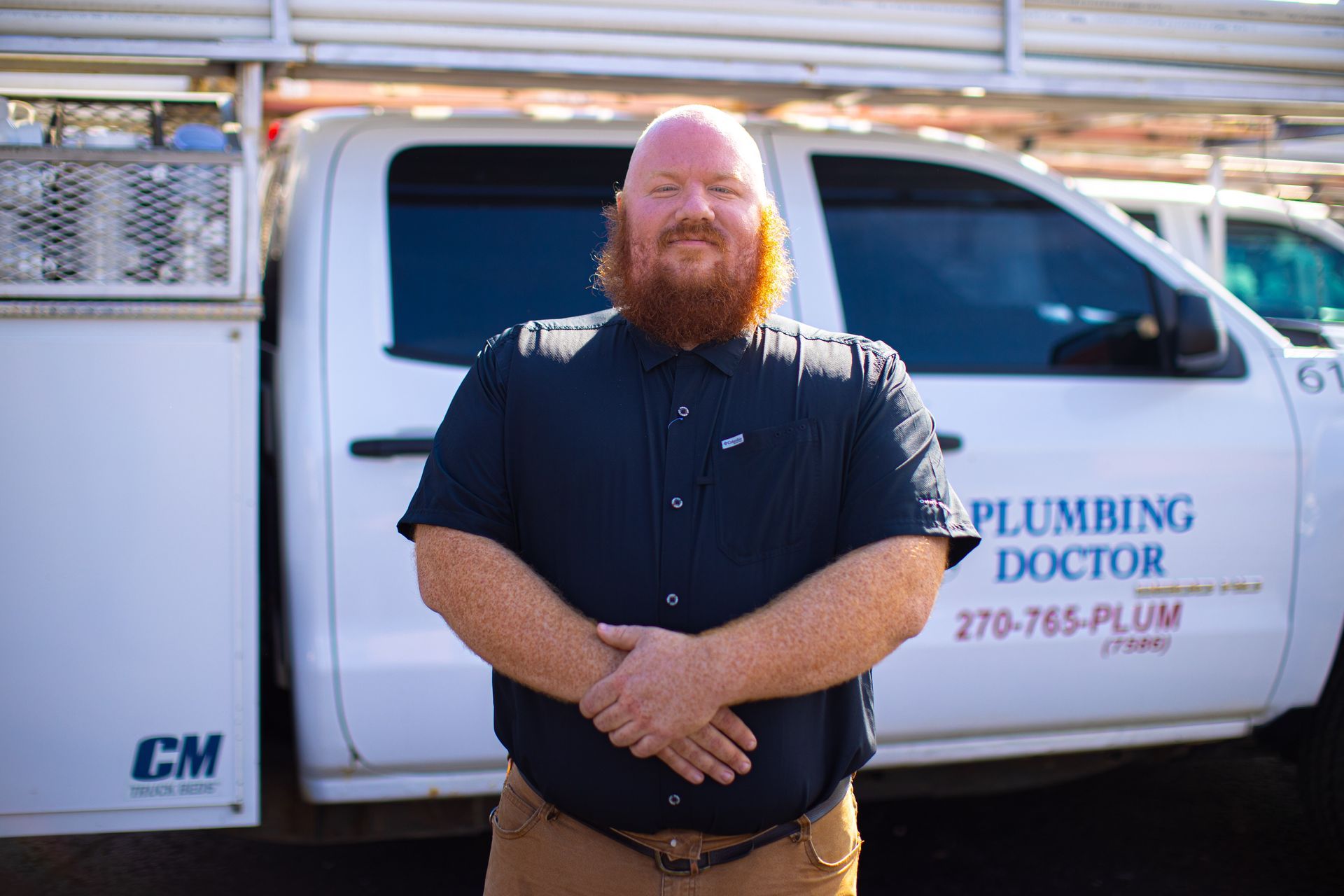 Man with red beard, arms crossed, stands in front of Plumbing Doctor truck.