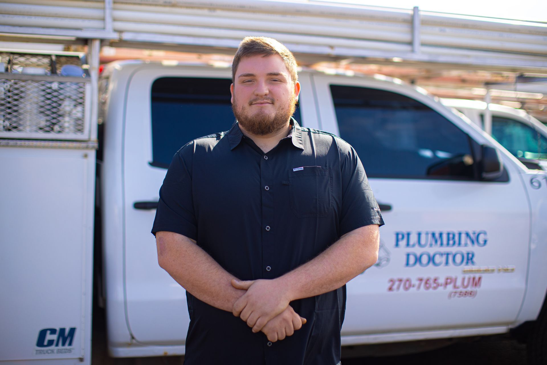 Man in black shirt stands in front of a white Plumbing Doctor truck.
