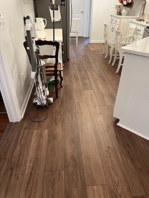 A kitchen with dark wood floors, a white countertop, and dining table with chairs.