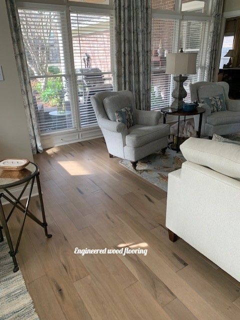 Living room with engineered wood flooring, white chairs, and window with patterned curtains.