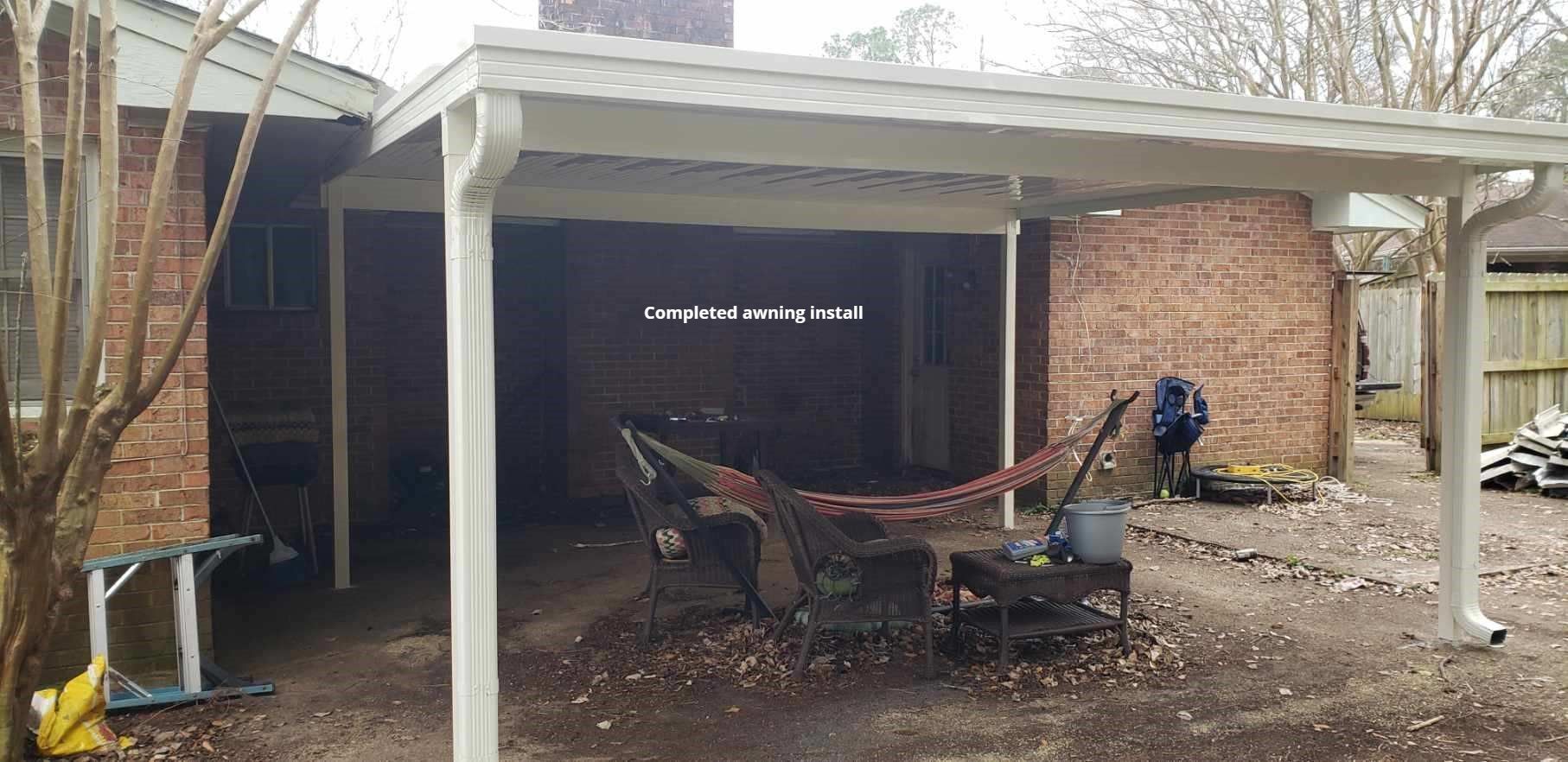 A carport attached to a brick home. A person works in the backyard.