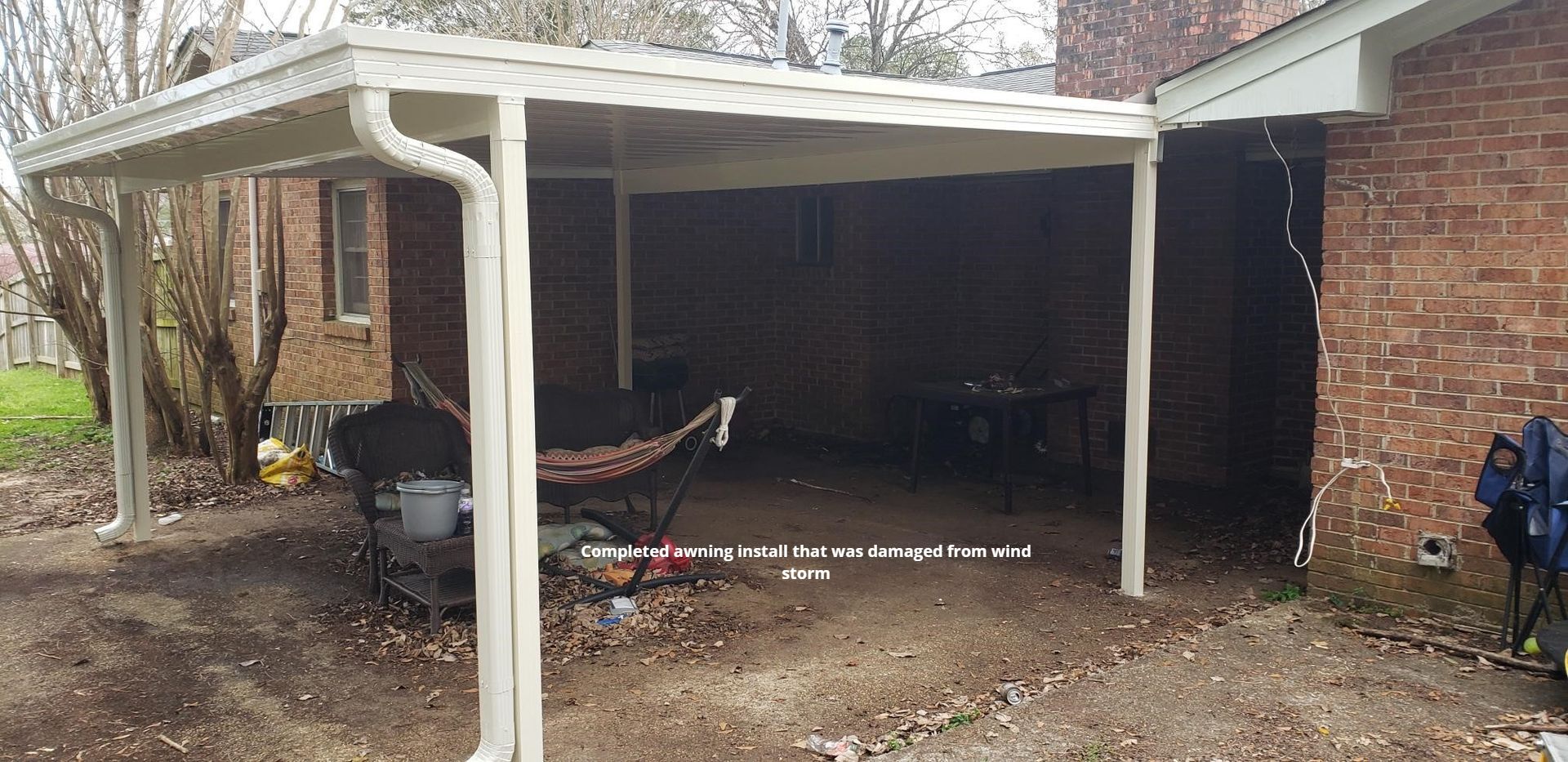 A covered patio attached to a brick home. A hammock and other items are visible underneath the shelter.