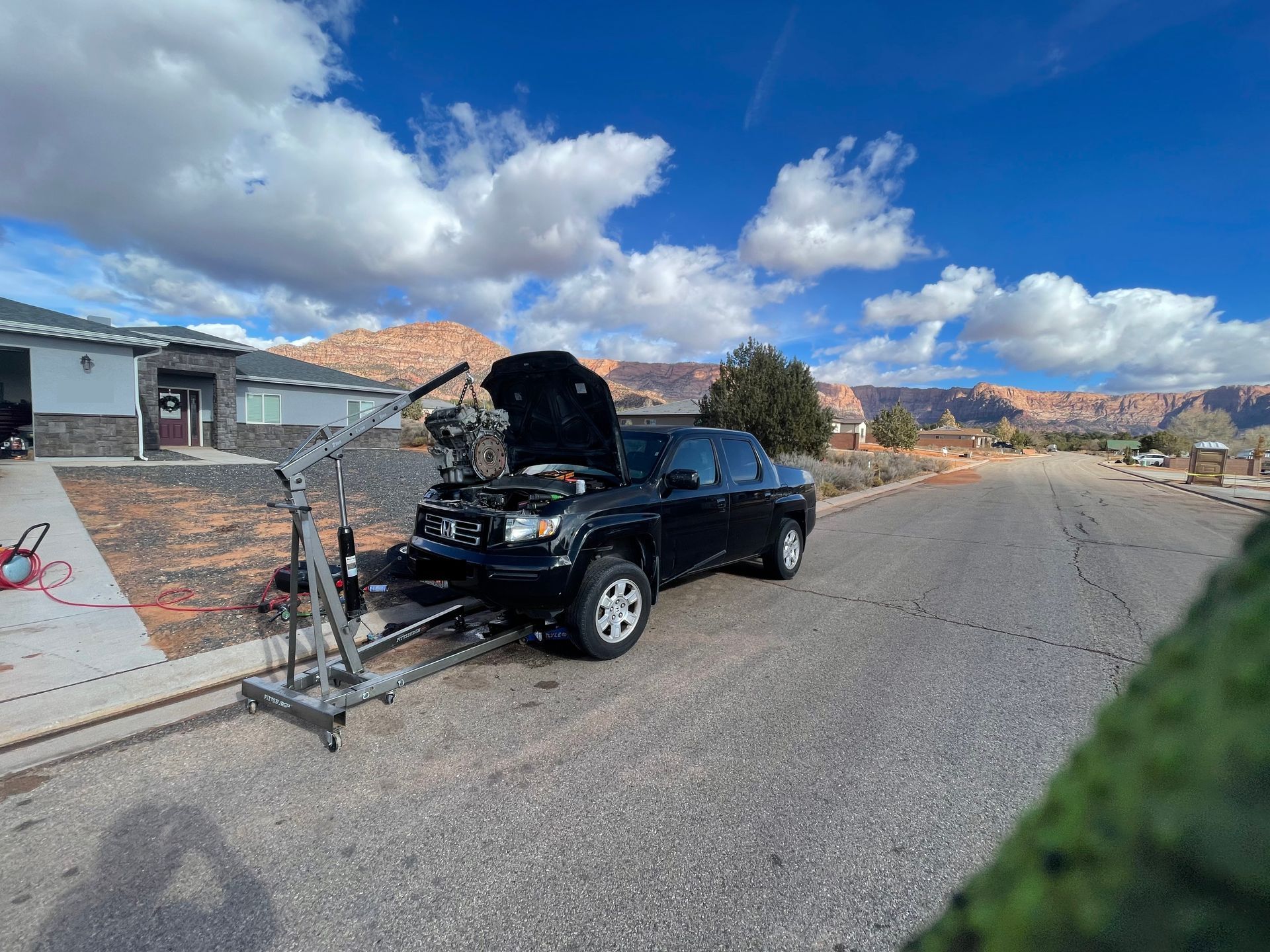 A black truck with its hood up is parked on the side of the road.
