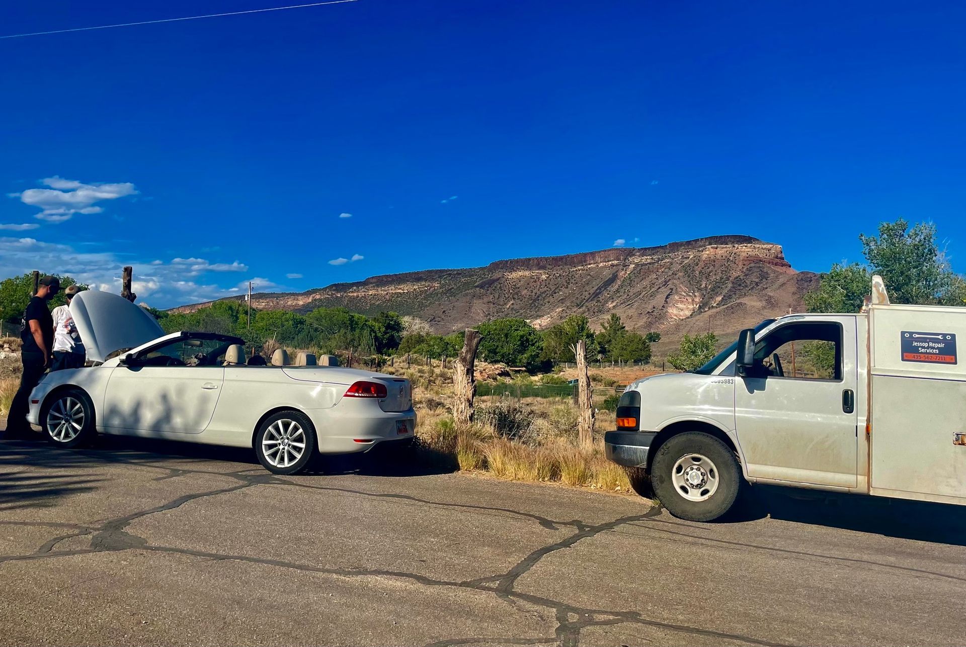 A man is standing next to a white car with the hood up.
