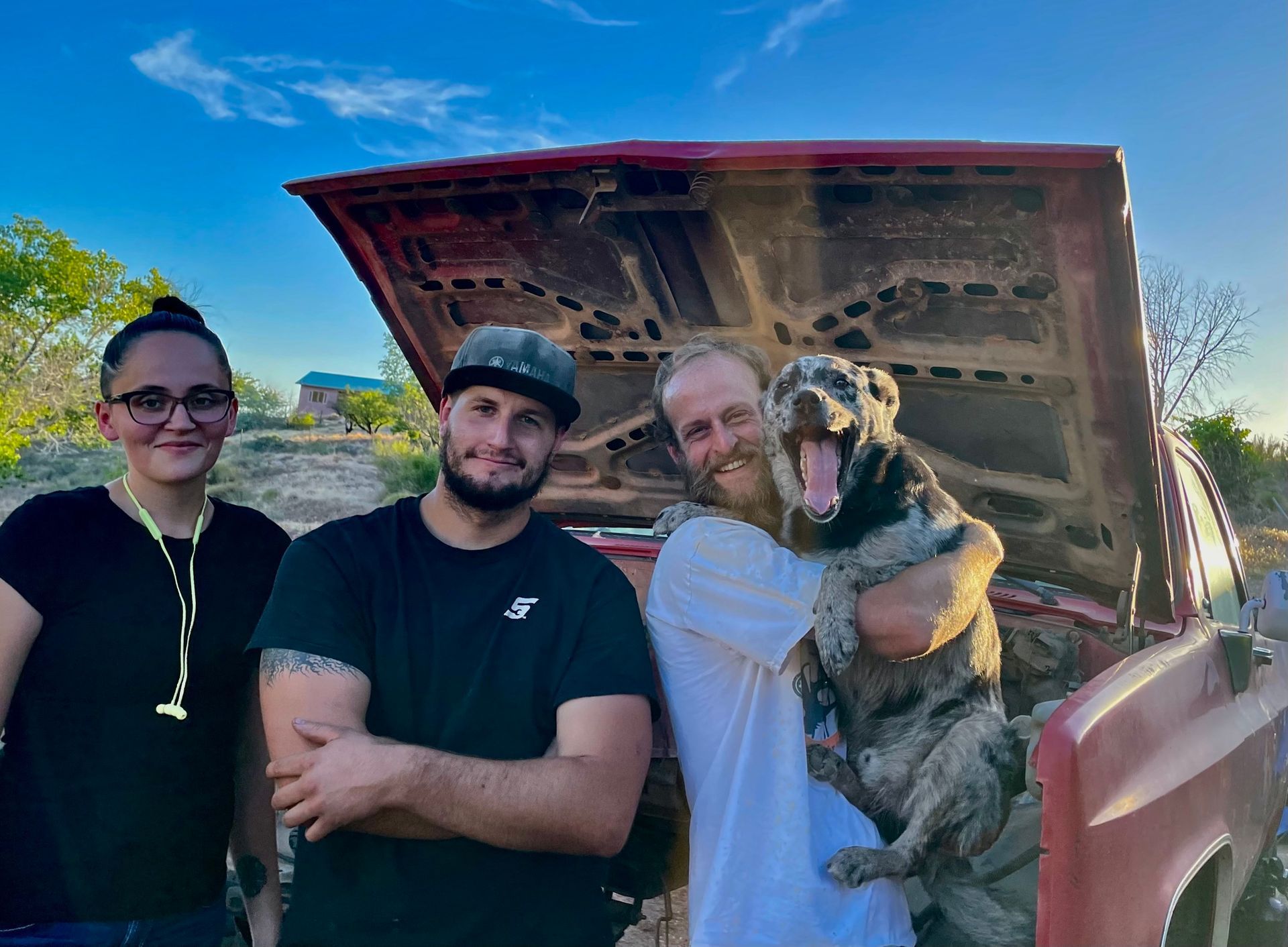 A group of people standing next to each other with a dog in the back of a truck.