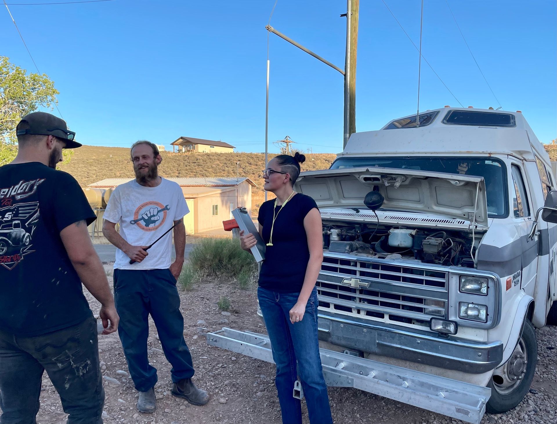 A group of people are standing in front of a van with the hood open.