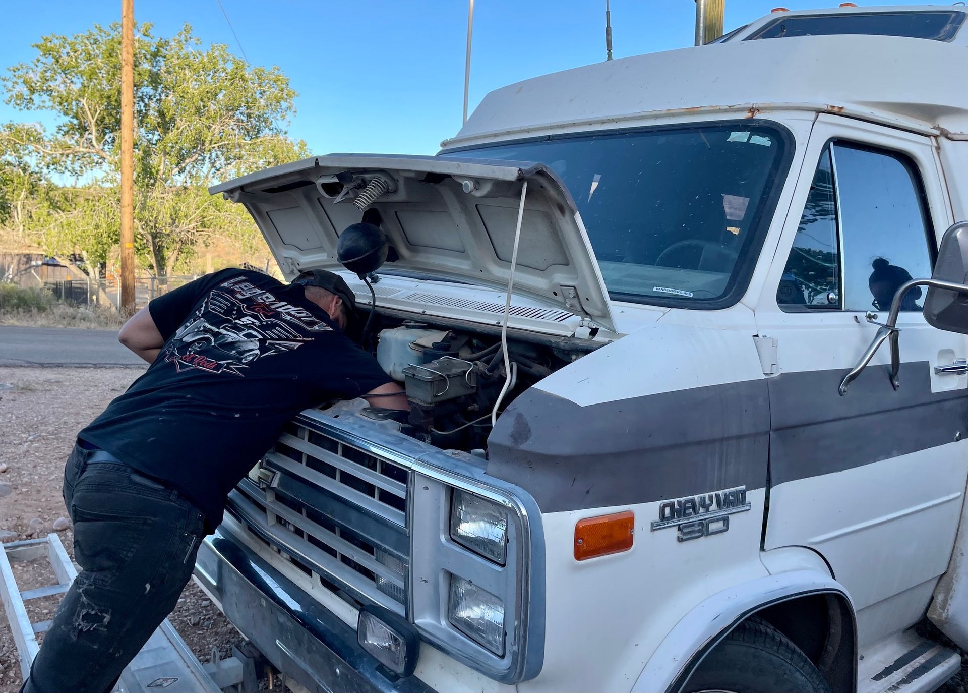 A man is looking under the hood of a white van.