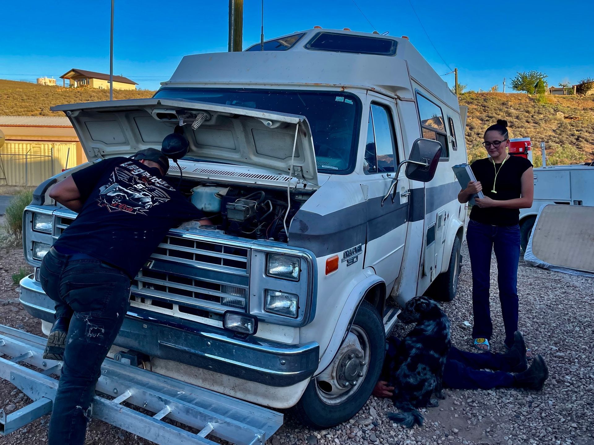 A man and a woman are working on a van with the hood open