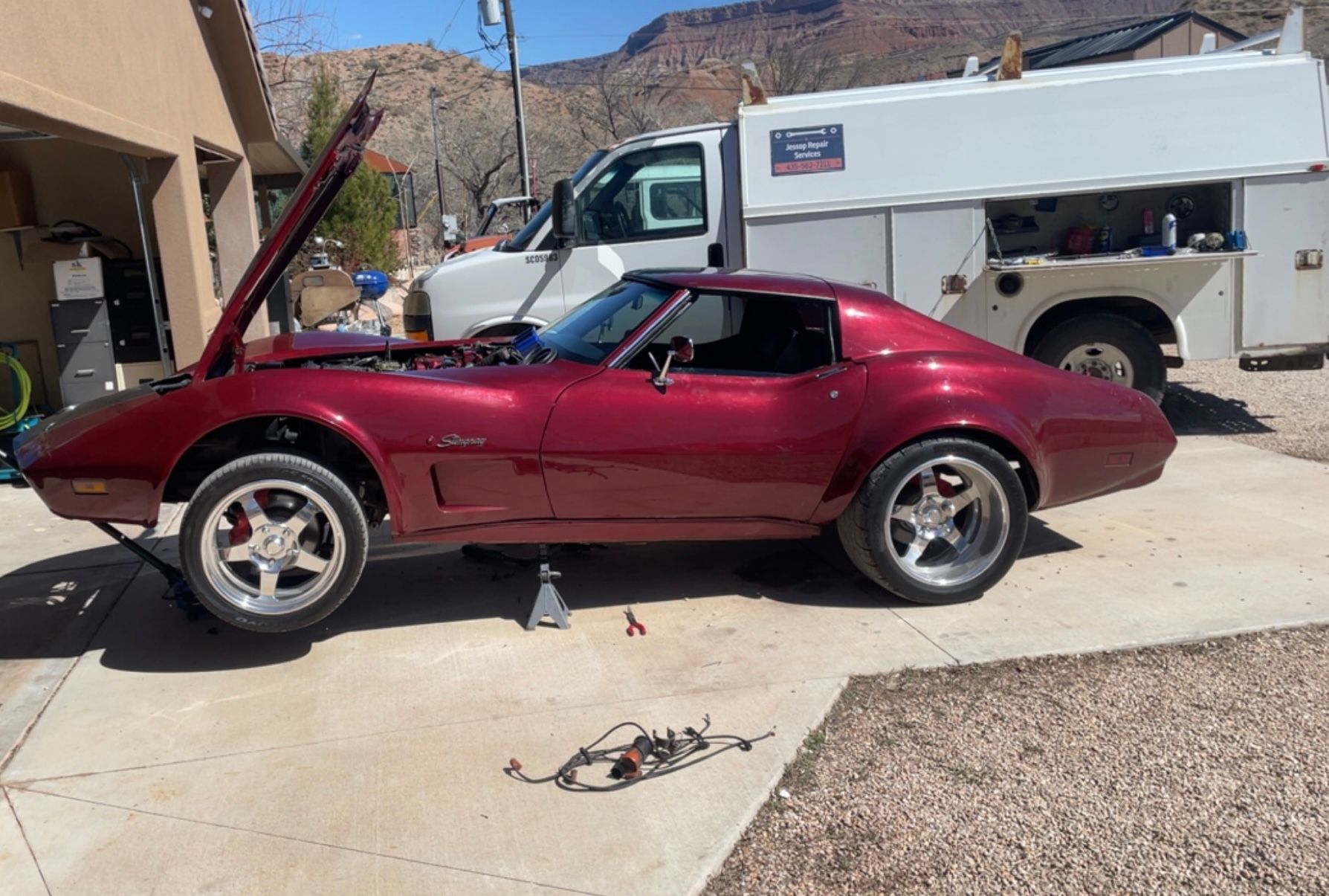 A red car with the hood up is parked in front of a white truck.