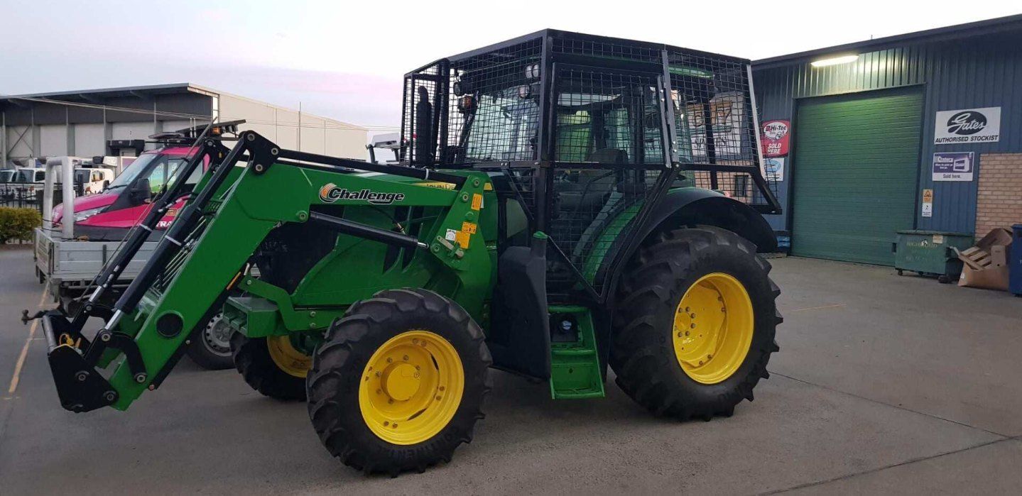 A Green Tractor With a Front Loader and Protective Cage is Parked Outside a Building — AWE Engineering in South Lismore, NSW