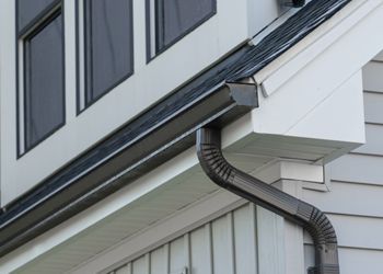 Dark gutters on a house with white siding and windows.