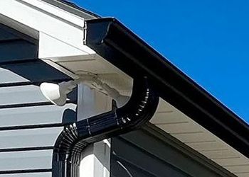 Black gutters attached to a house, with a curved downspout against a blue sky.