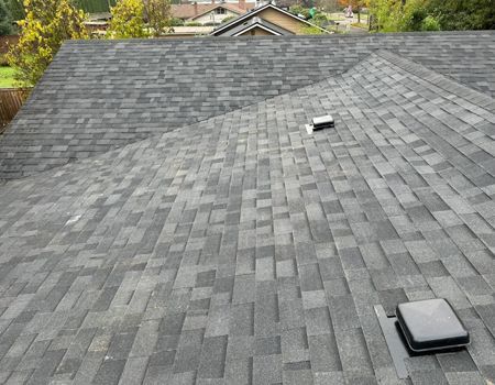Gray asphalt shingle roof with two vents, angled view.