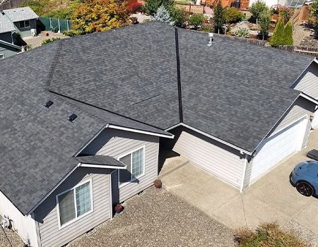 Gray-shingled roof on a light gray house with two garage doors and a blue car parked outside.