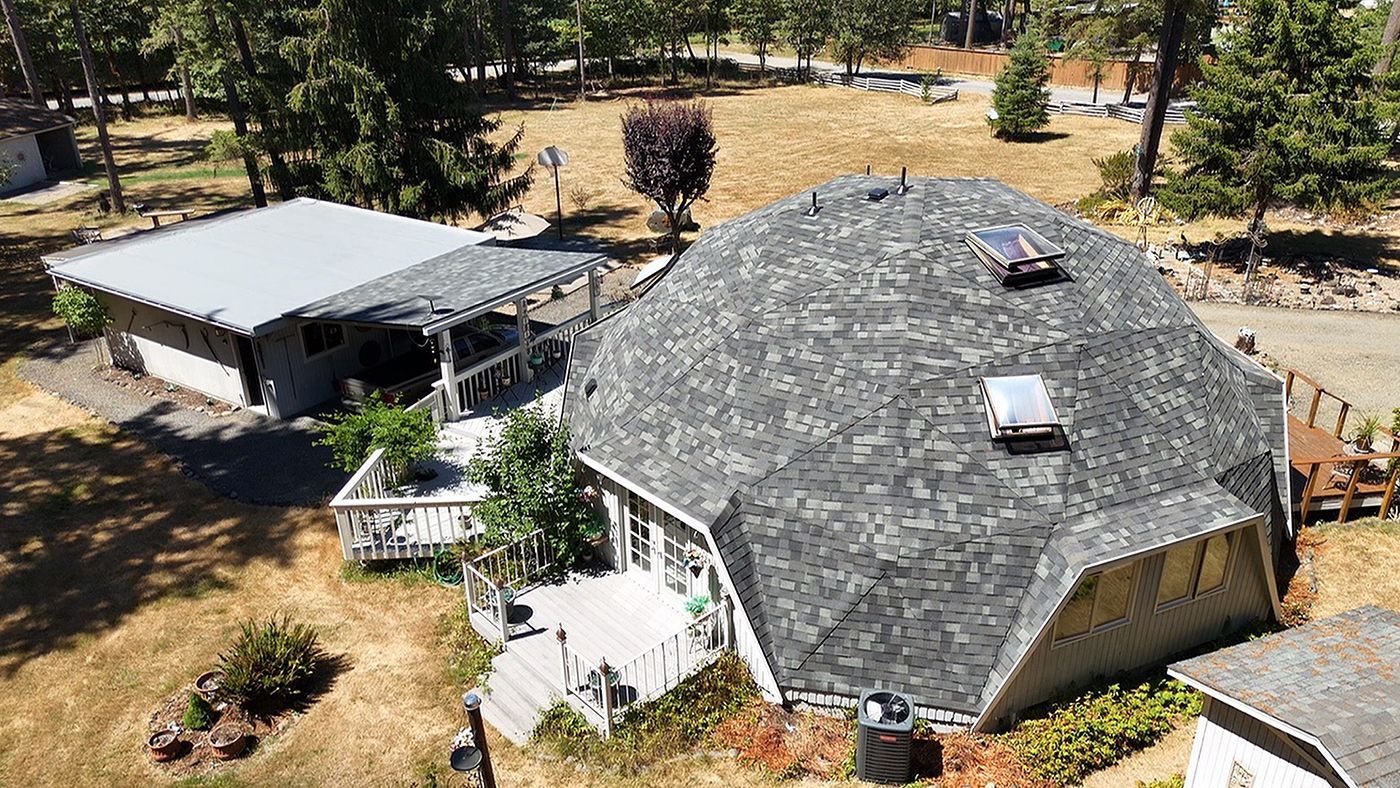 Dome-shaped house with gray shingle roof and attached deck, next to a smaller rectangular building with a covered porch.