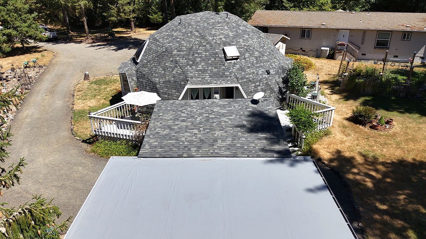 Dome-shaped house with gray shingle roof, white trim, and a long gray flat roof. Outdoors on a sunny day.