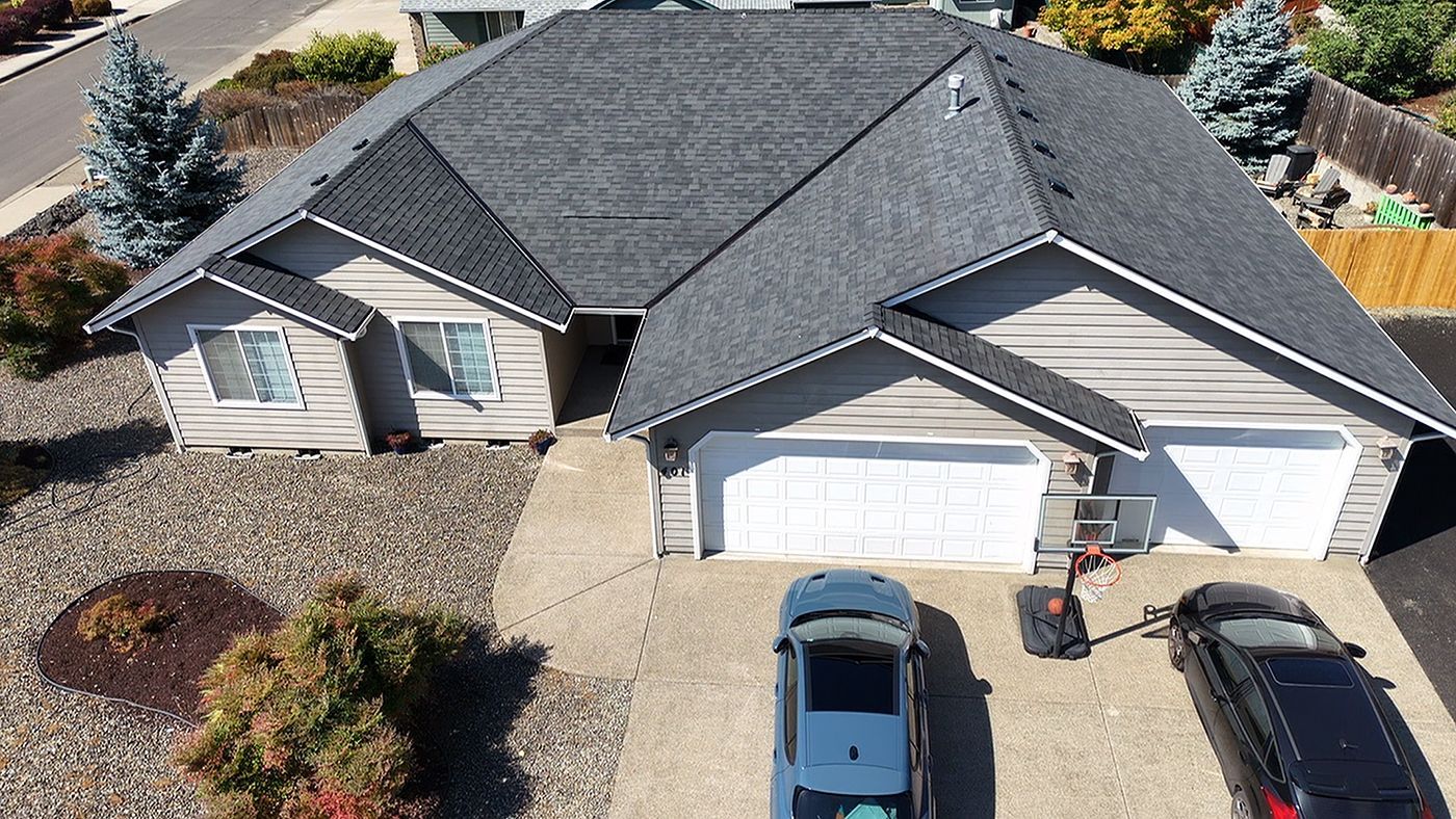 An aerial view of a single-story house with a grey roof, beige siding, a two-car garage, and two parked cars.