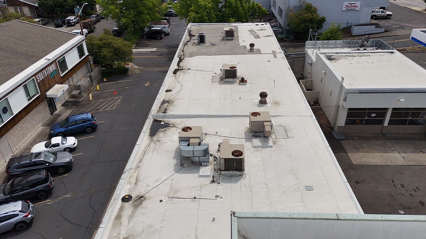 View of a flat commercial roof with HVAC units, surrounded by buildings and parked vehicles.