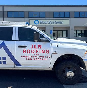 White JLN Roofing truck in front of a building with the sign