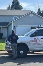 A man is standing next to a roofing truck in front of a house.