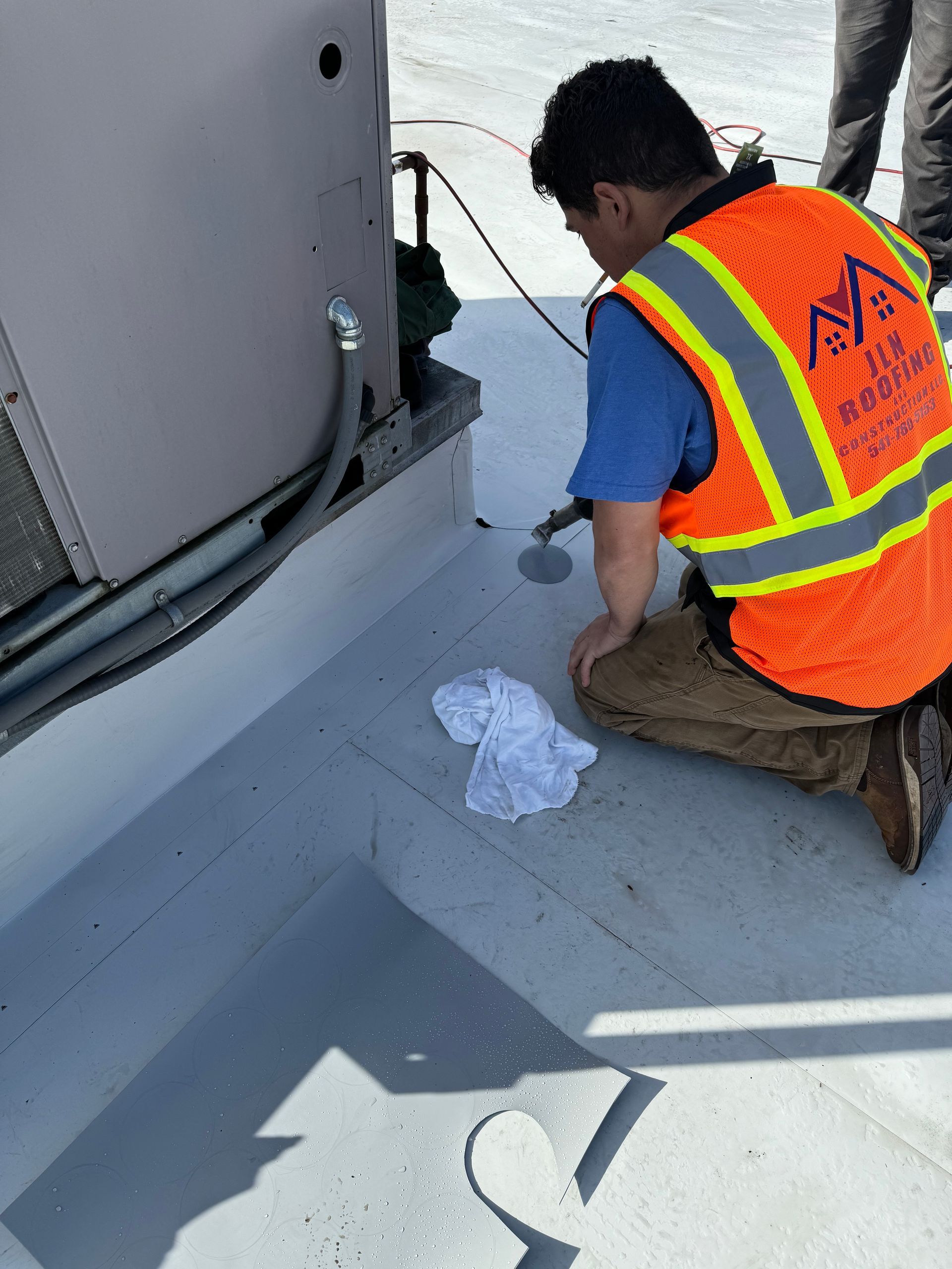 A man in an orange vest is working on a roof
